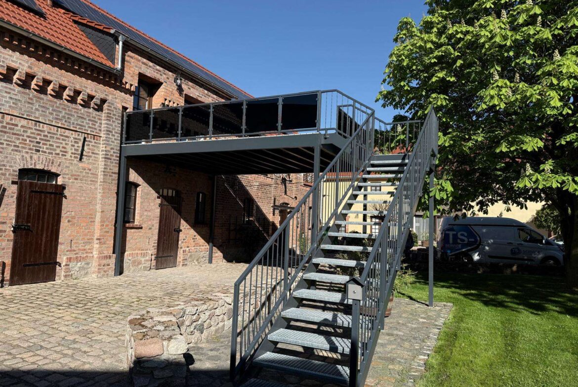 Metal exterior staircase leading to a second-story deck attached to a brick building with solar panels on the roof.