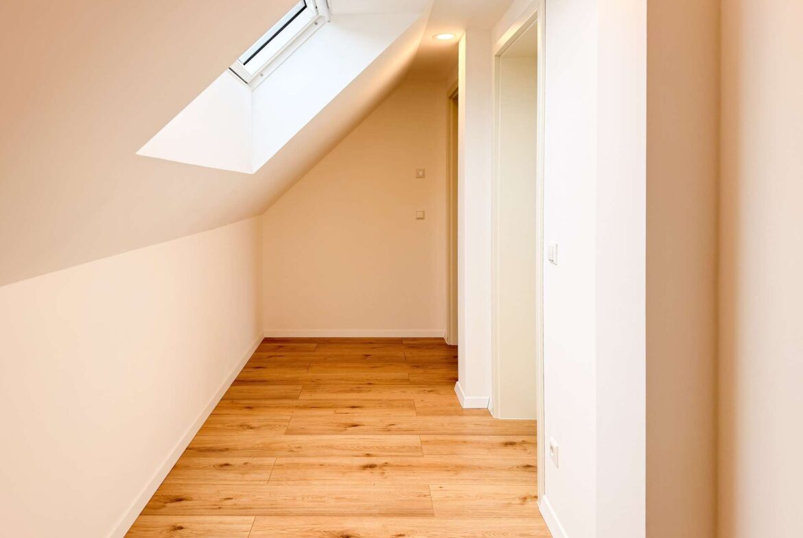 Bright narrow hallway with a sloped ceiling and skylight, white walls and warm wooden flooring there