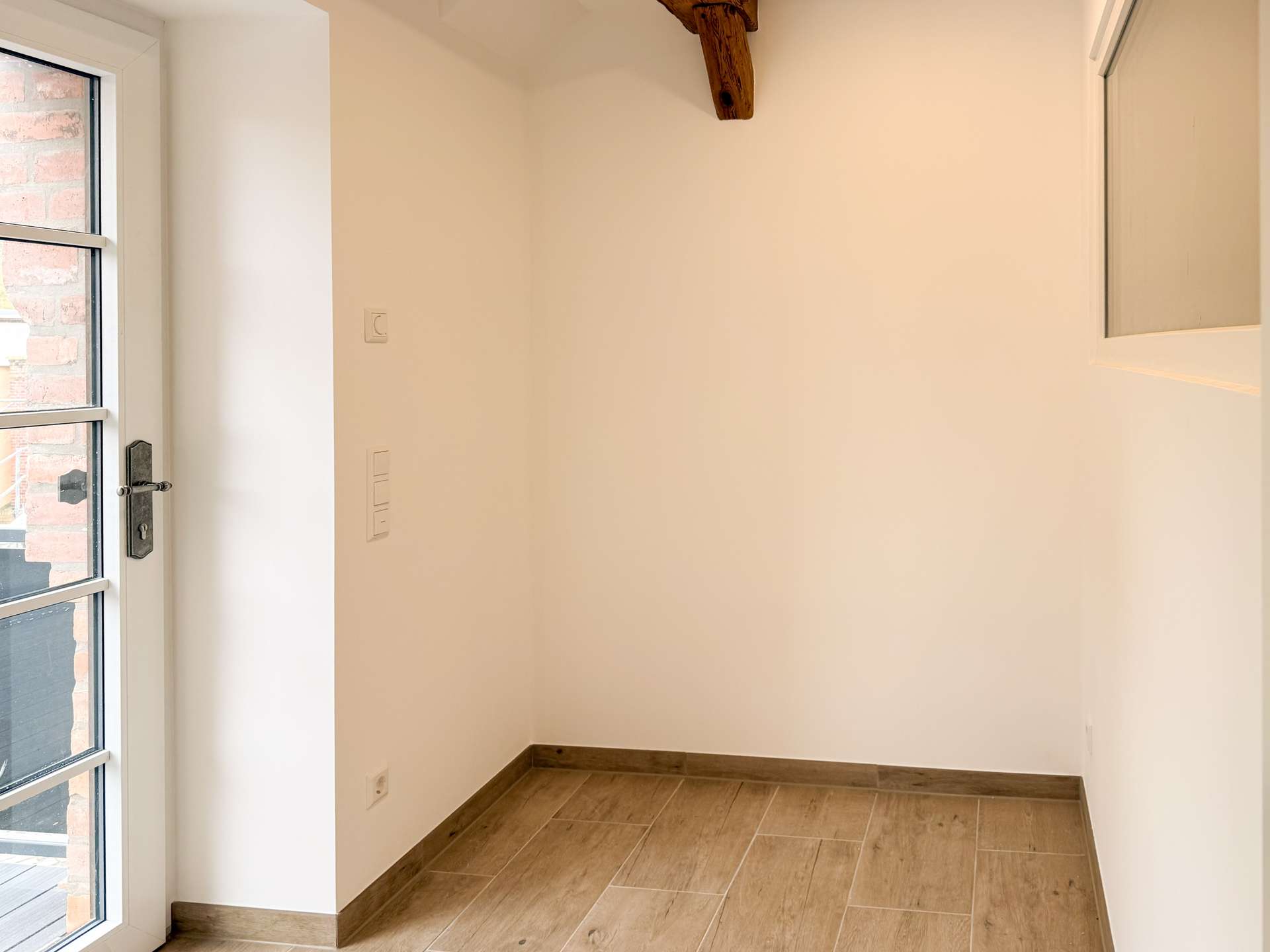 Narrow entryway with a glass-panel door on the left, white walls, and a wooden ceiling beam.