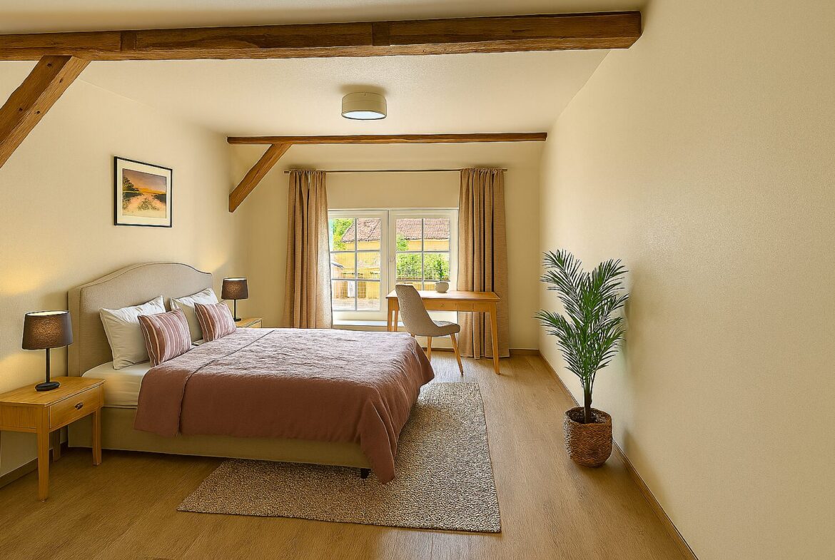 Cozy hotel bedroom with a king bed, two bedside lamps, and a wooden desk by a window with beige curtains.