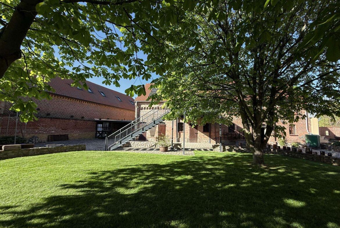 Brick building with a metal exterior staircase in a sunny courtyard, shaded by a large leafy tree above.
