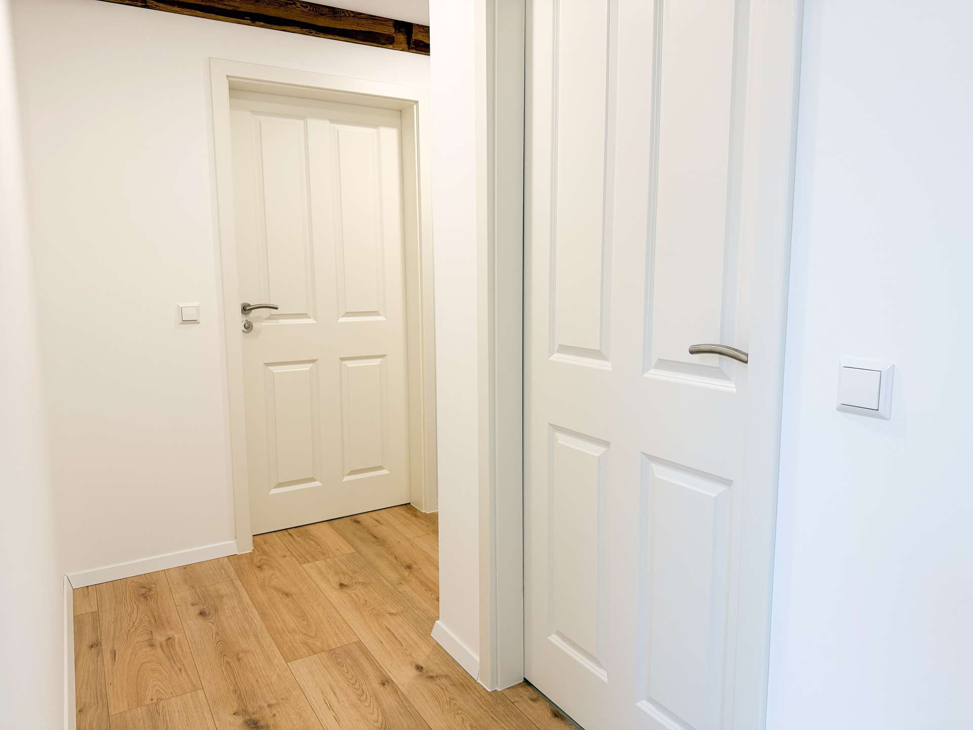 Narrow white hallway with light wood flooring, a white paneled interior door on the left and white sliding closet doors on the right Area looks clean and bright.