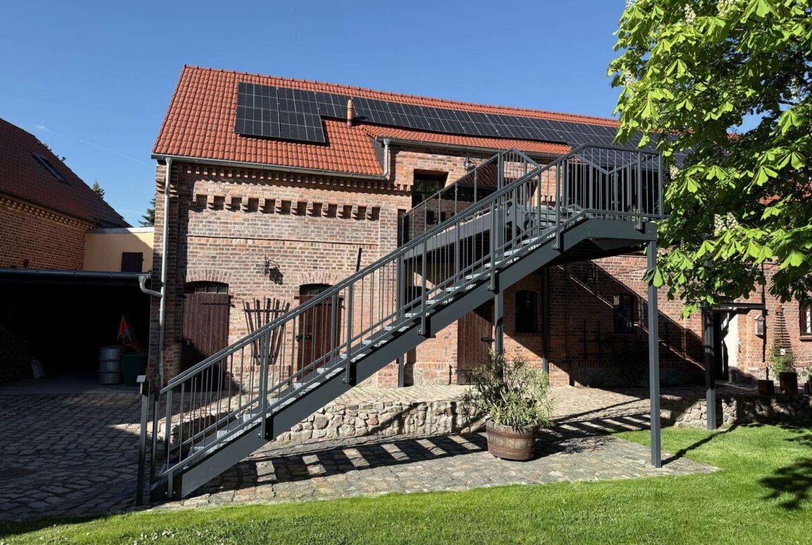 Brick building with red-tiled roof and solar panels, connected by a metal exterior staircase.