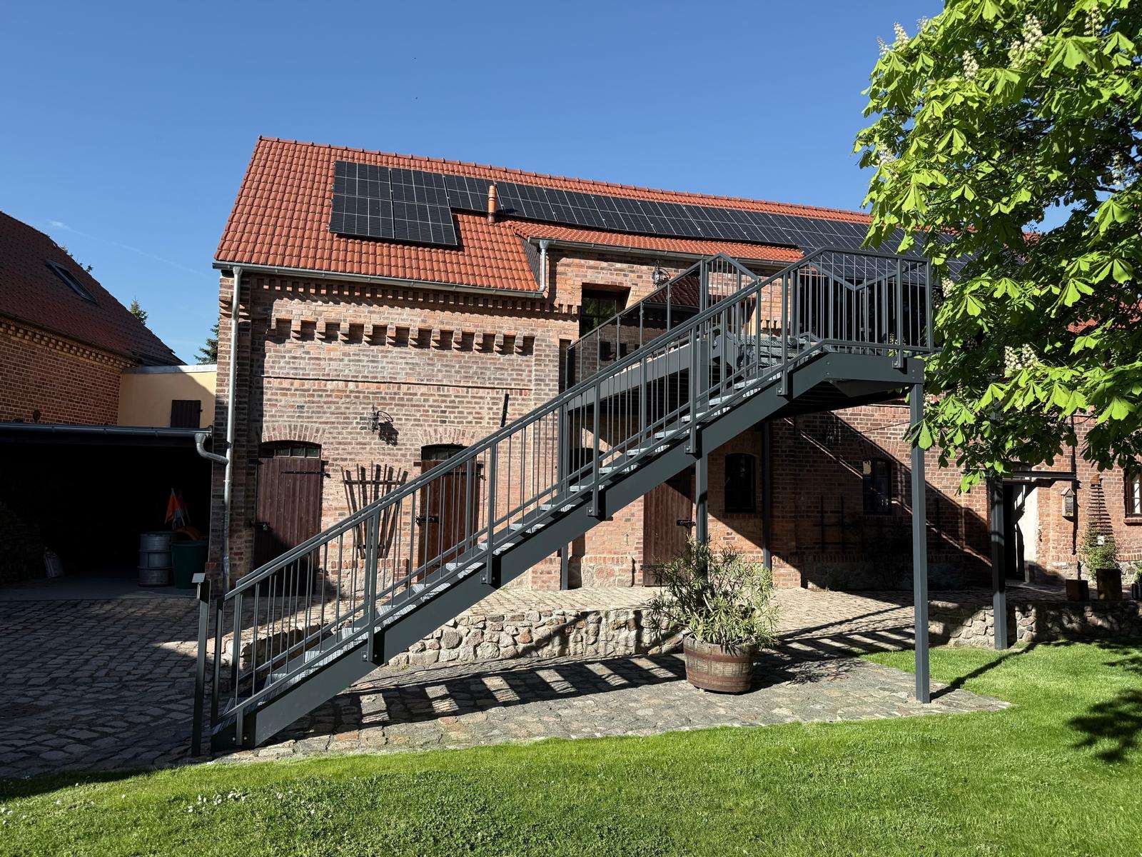 Brick building with red-tiled roof and solar panels, connected by a metal exterior staircase.