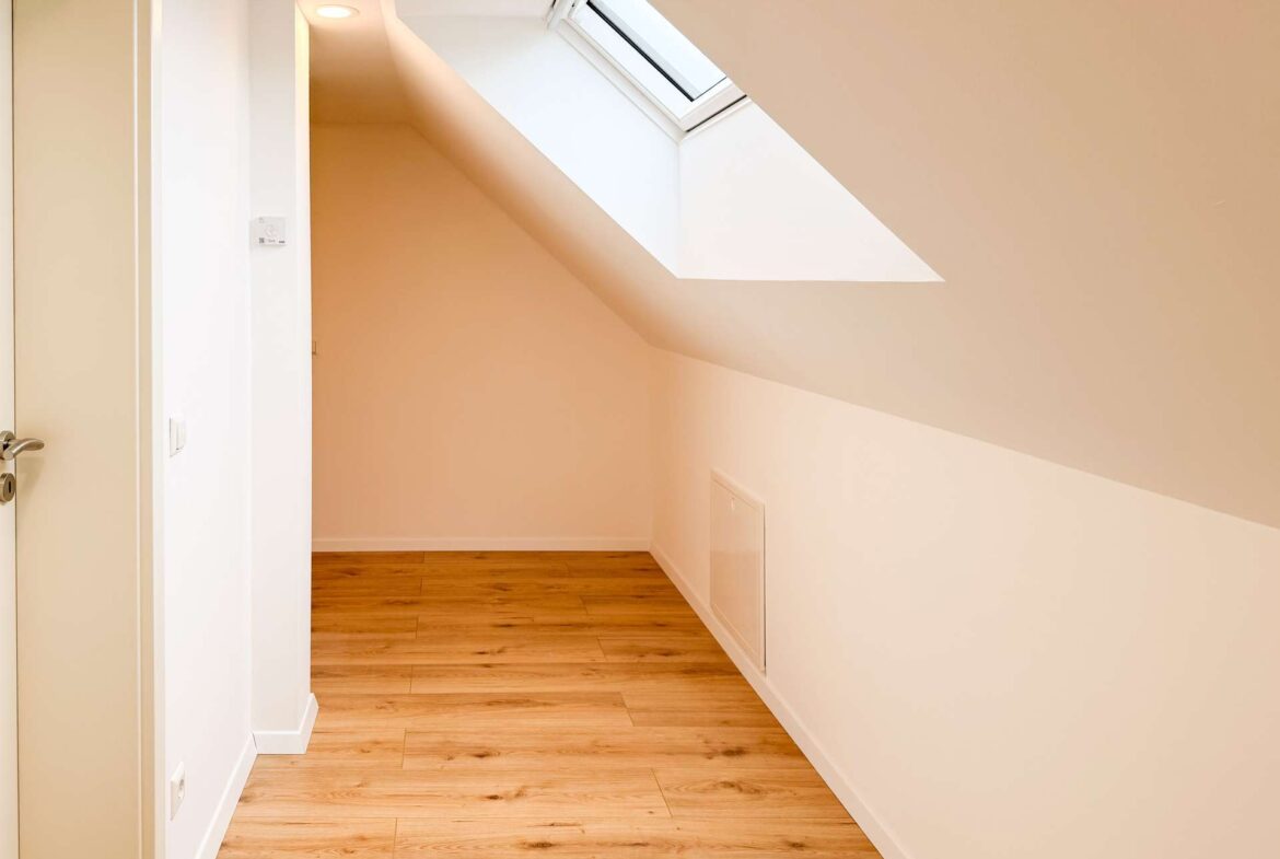 Bright hallway with angled white walls and a skylight letting in natural light, wooden floor.