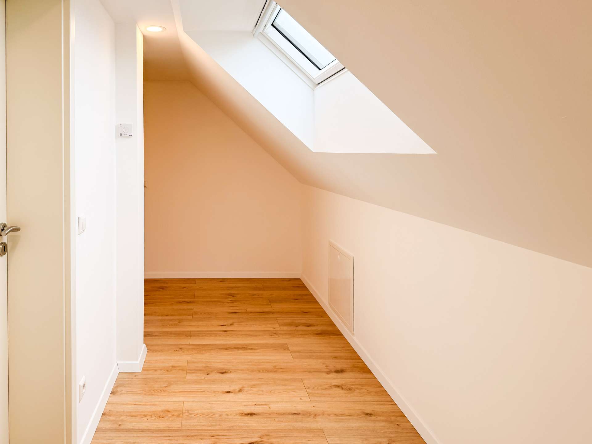 Bright hallway with angled white walls and a skylight letting in natural light, wooden floor.