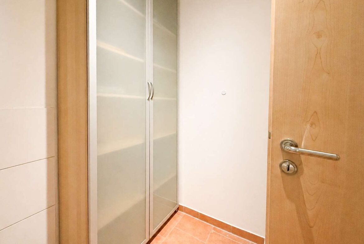 Narrow hallway with a wooden door ajar on the right and a frosted glass wardrobe on the left, tiled floor beneath a peachy floor.