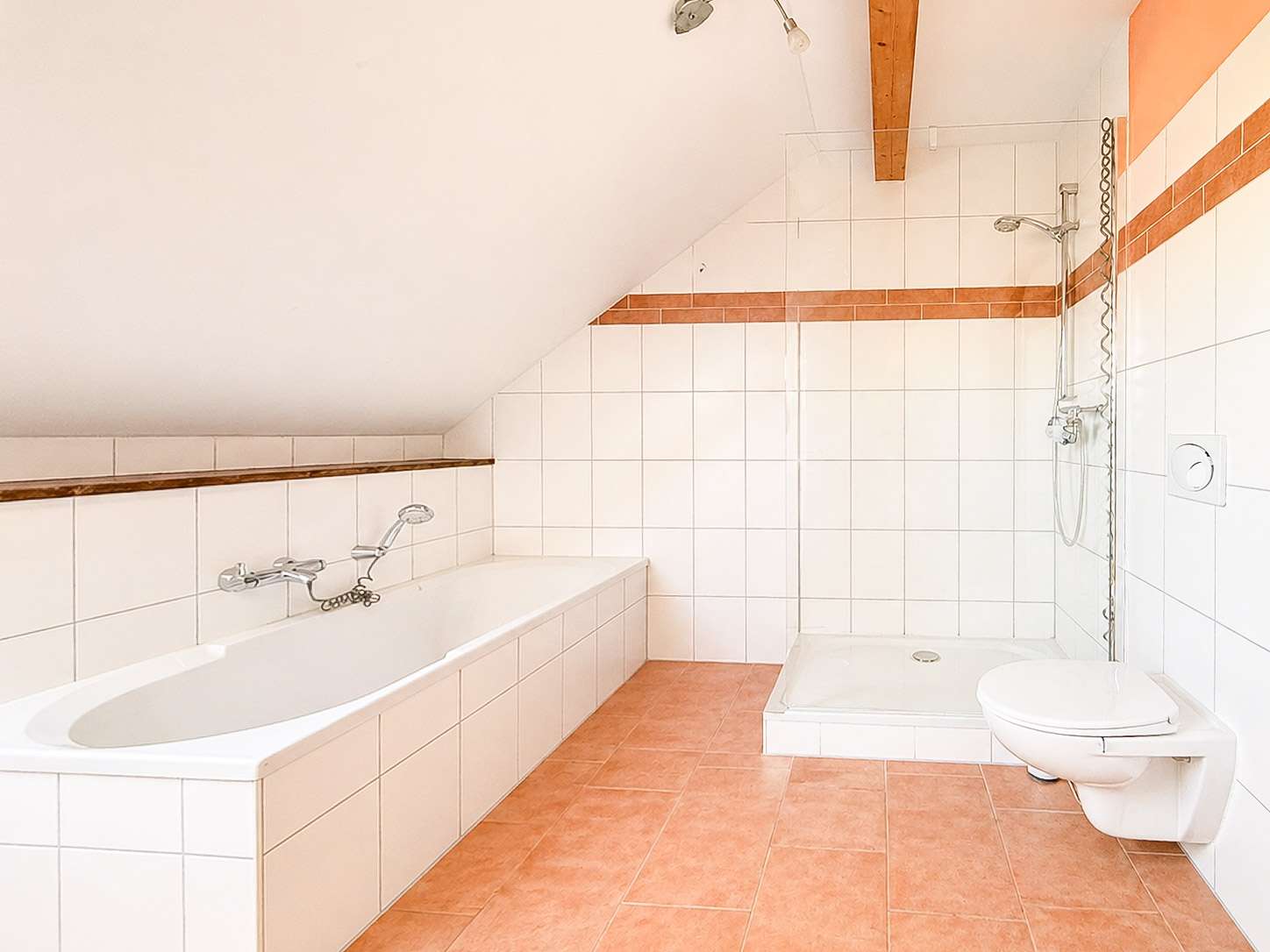 Bathroom with a white bathtub along the left wall, sloped ceiling, and a walk-in shower area on the right; peach floor tiles and orange-brown wall stripes.