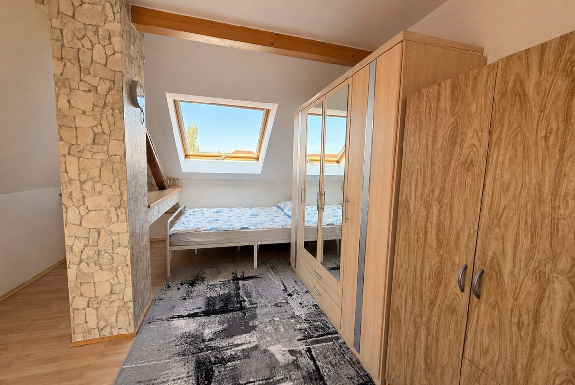 Bedroom with a single bed under a sloped ceiling and skylight window, wood wardrobe, and stone pillar feature wall.