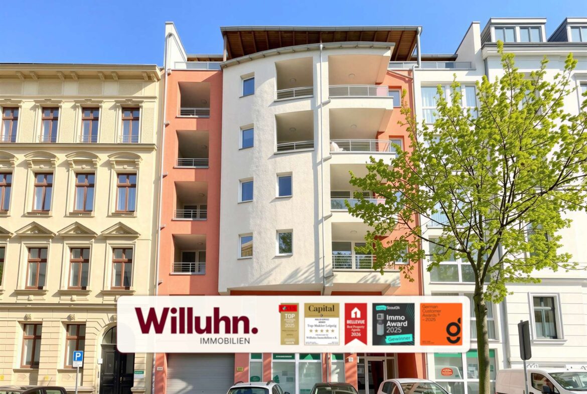 Colorful residential building fronts with a storefront sign 'Willuhn Immobilien' in the foreground and a tree on the right under a blue sky.