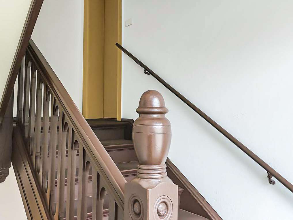 Wooden staircase with an ornate newel post and brown handrail in a bright hallway