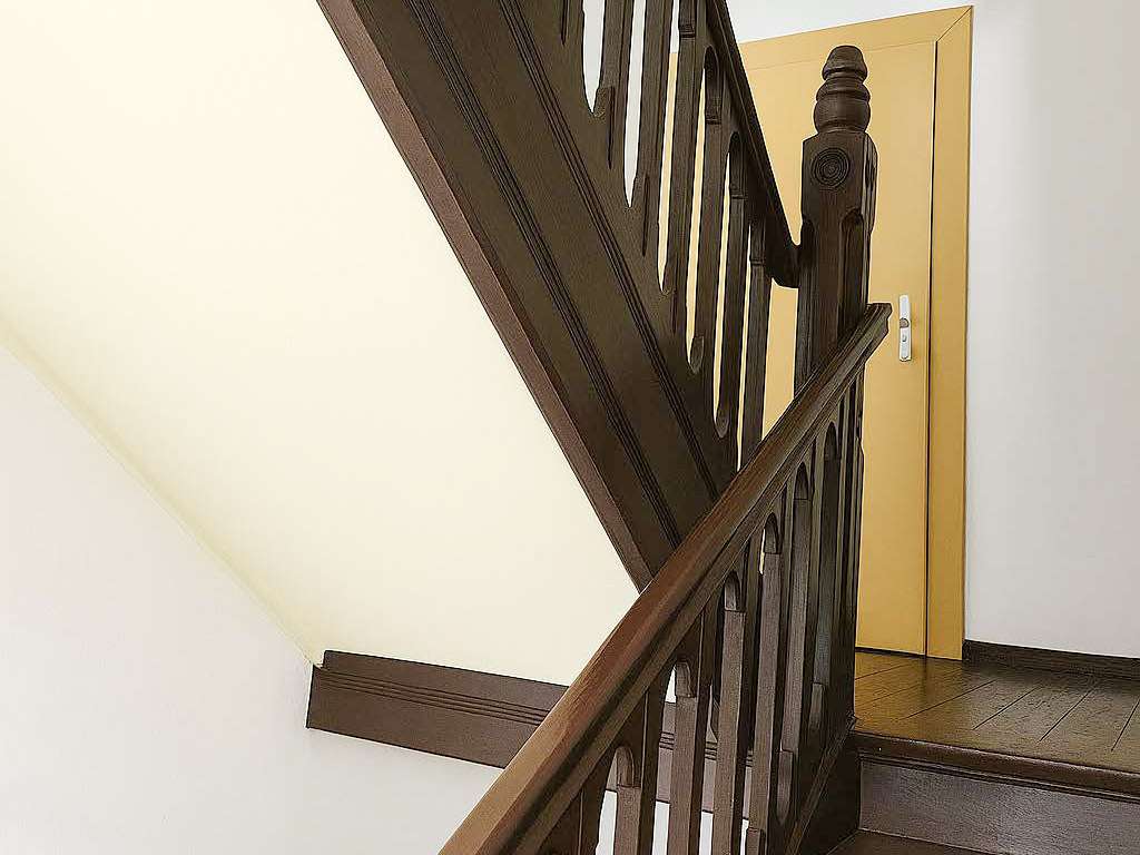 Dark wooden staircase railing and balusters ascend toward a mustard-yellow door on the landing.