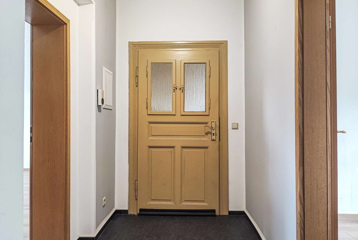 Narrow hallway with white walls and a beige/gold door at the far end, featuring two frosted glass panels.