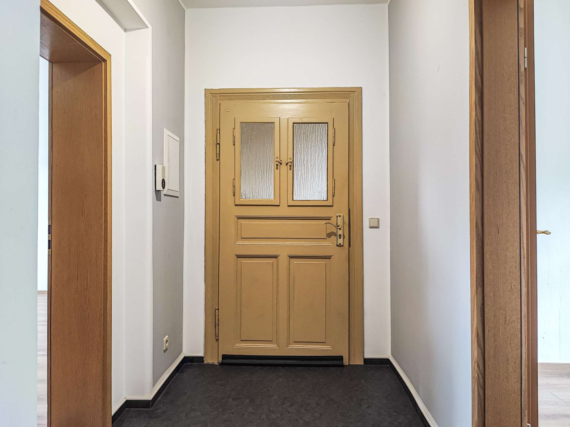 Narrow hallway with white walls and a beige/gold door at the far end, featuring two frosted glass panels.