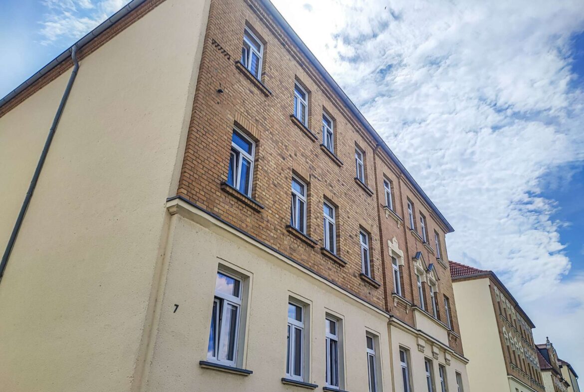 Angle view of a brick apartment building with multiple white-framed windows against a blue, cloudy sky.