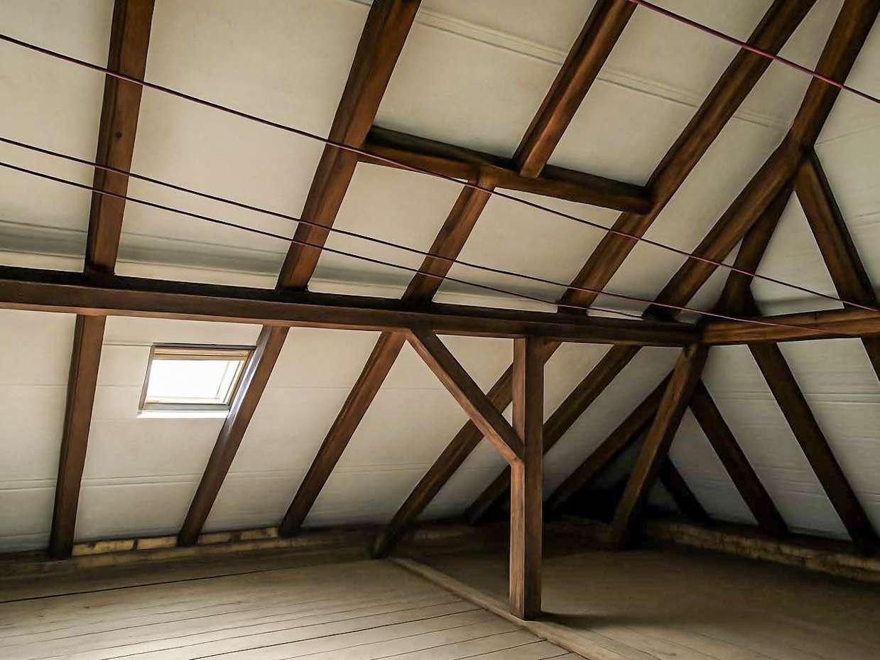 Attic with exposed wooden roof trusses, slanted ceiling, and a small skylight window letting in light, empty space below