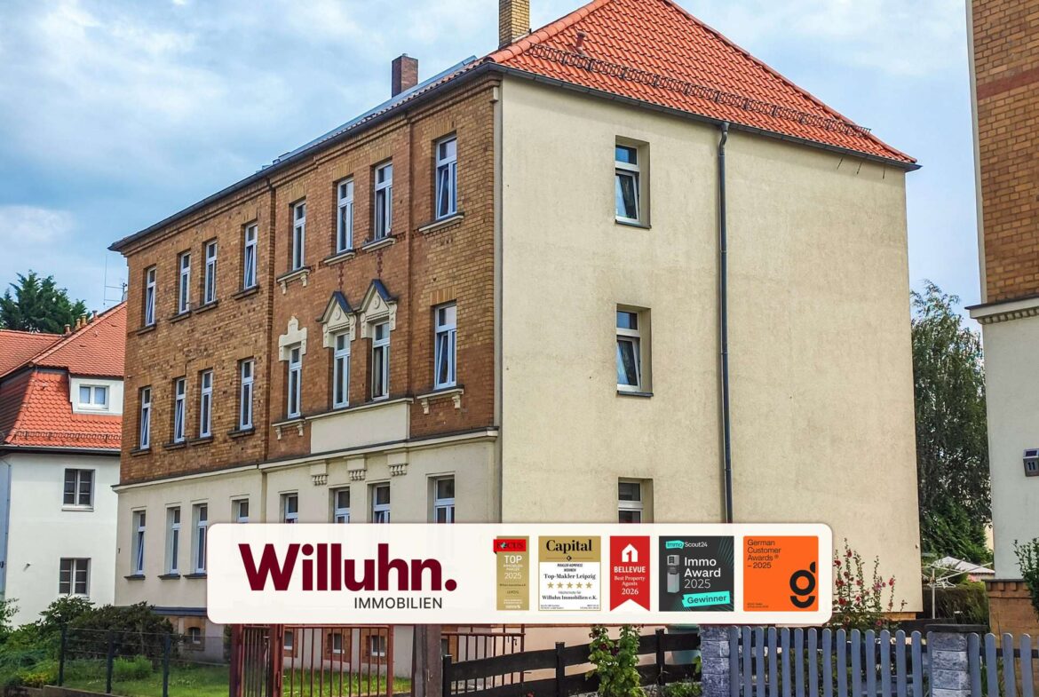 Facade of a multi-story brick apartment building with a red tiled roof and a large Willuhn Immobilien sign in the foreground, displaying award logos.