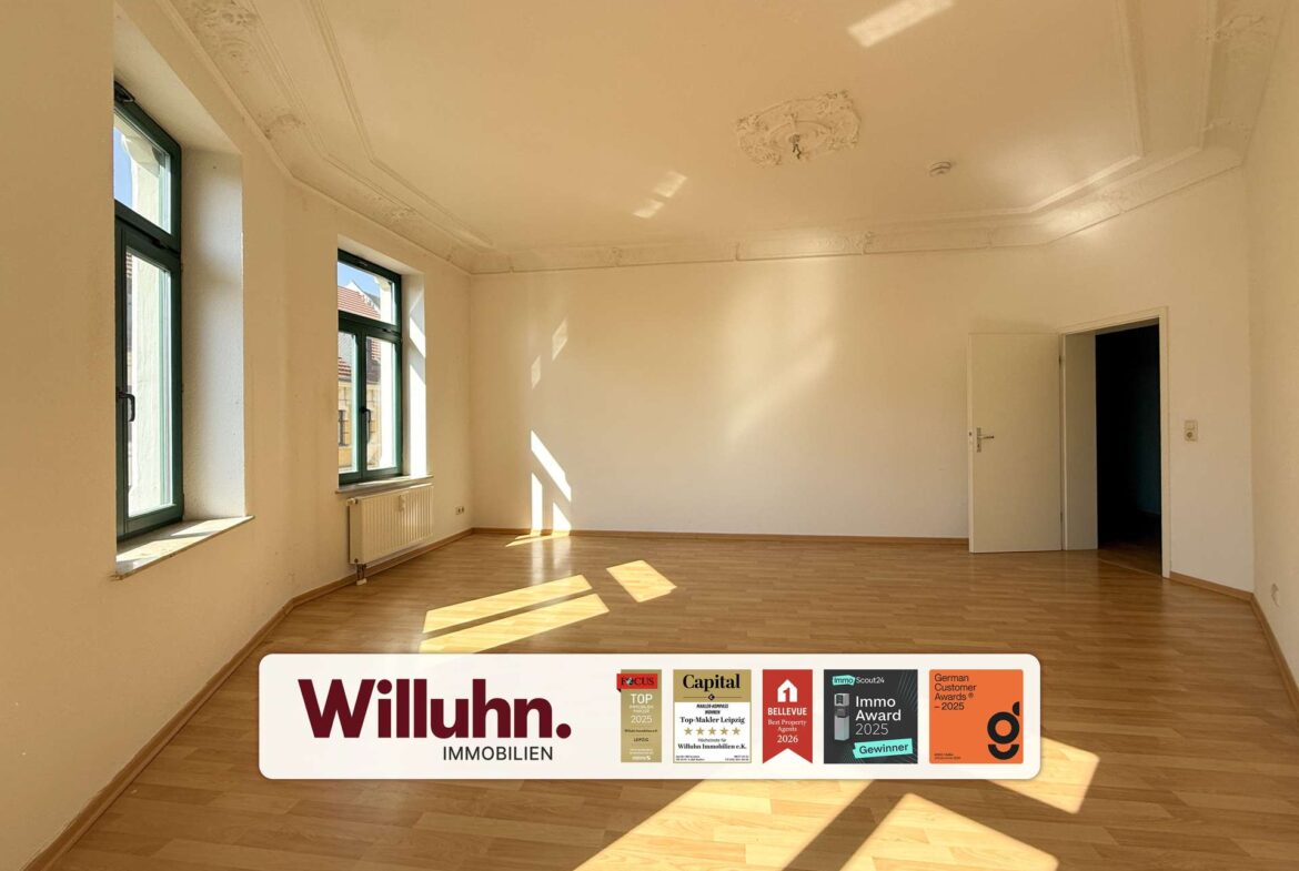 Bright empty room with tall green-framed windows, light wood floor, and decorative ceiling molding; doorway on the right.
