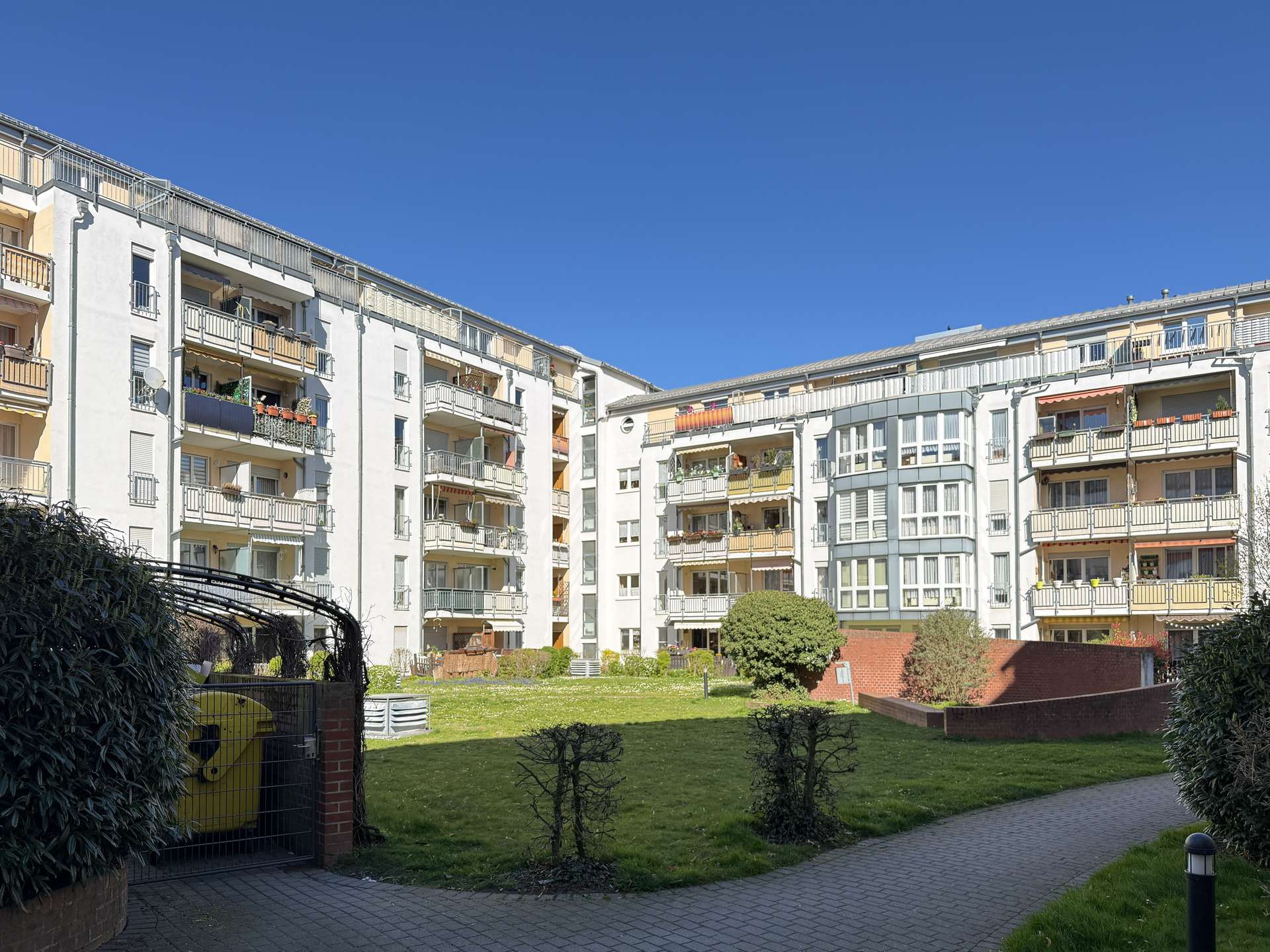 Apartment buildings with many balconies overlooking a green courtyard under a clear blue sky.