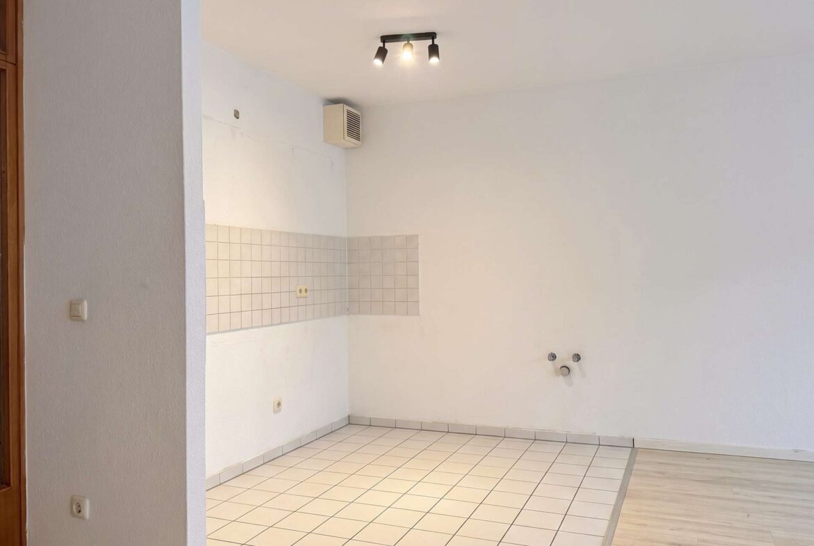 Empty kitchen corner with white tiled backsplash, outlets, and a three-bulb ceiling light; vent on the wall above.