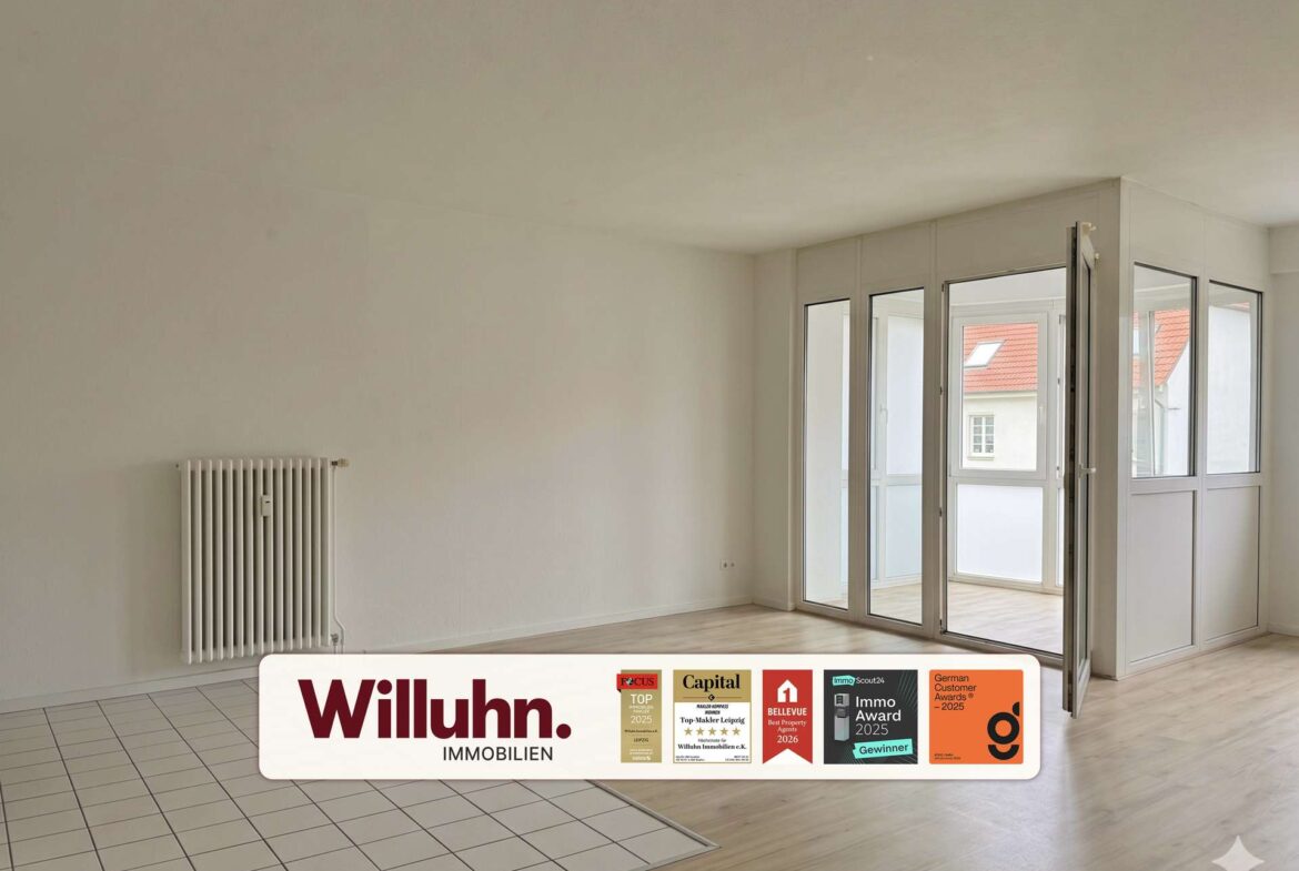 Empty living room with white walls, a radiator on the left, and large glass doors opening to a balcony; foreground shows a Willuhn Immobilien sign.
