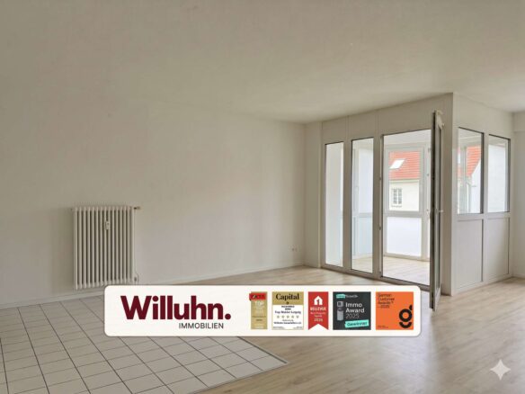 Empty living room with white walls, a radiator on the left, and large glass doors opening to a balcony; foreground shows a Willuhn Immobilien sign.