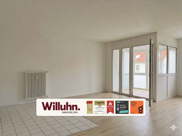 Empty living room with white walls, a radiator on the left, and large glass doors opening to a balcony; foreground shows a Willuhn Immobilien sign.