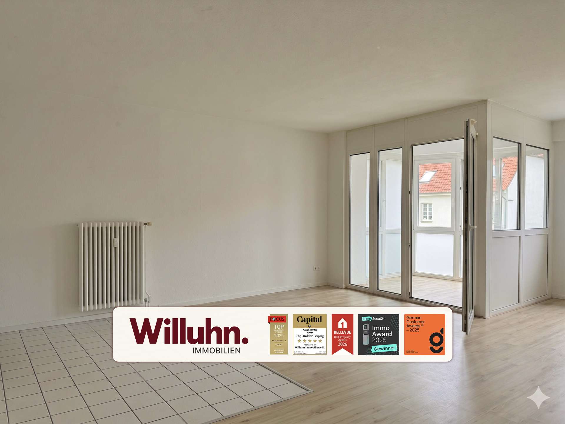Empty living room with white walls, a radiator on the left, and large glass doors opening to a balcony; foreground shows a Willuhn Immobilien sign.