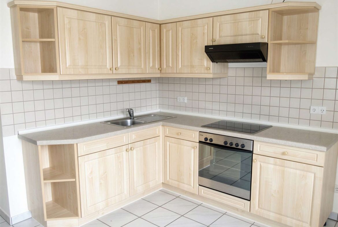 L-shaped kitchen with light wood cabinets, open shelves, and a black range hood above a stove and oven