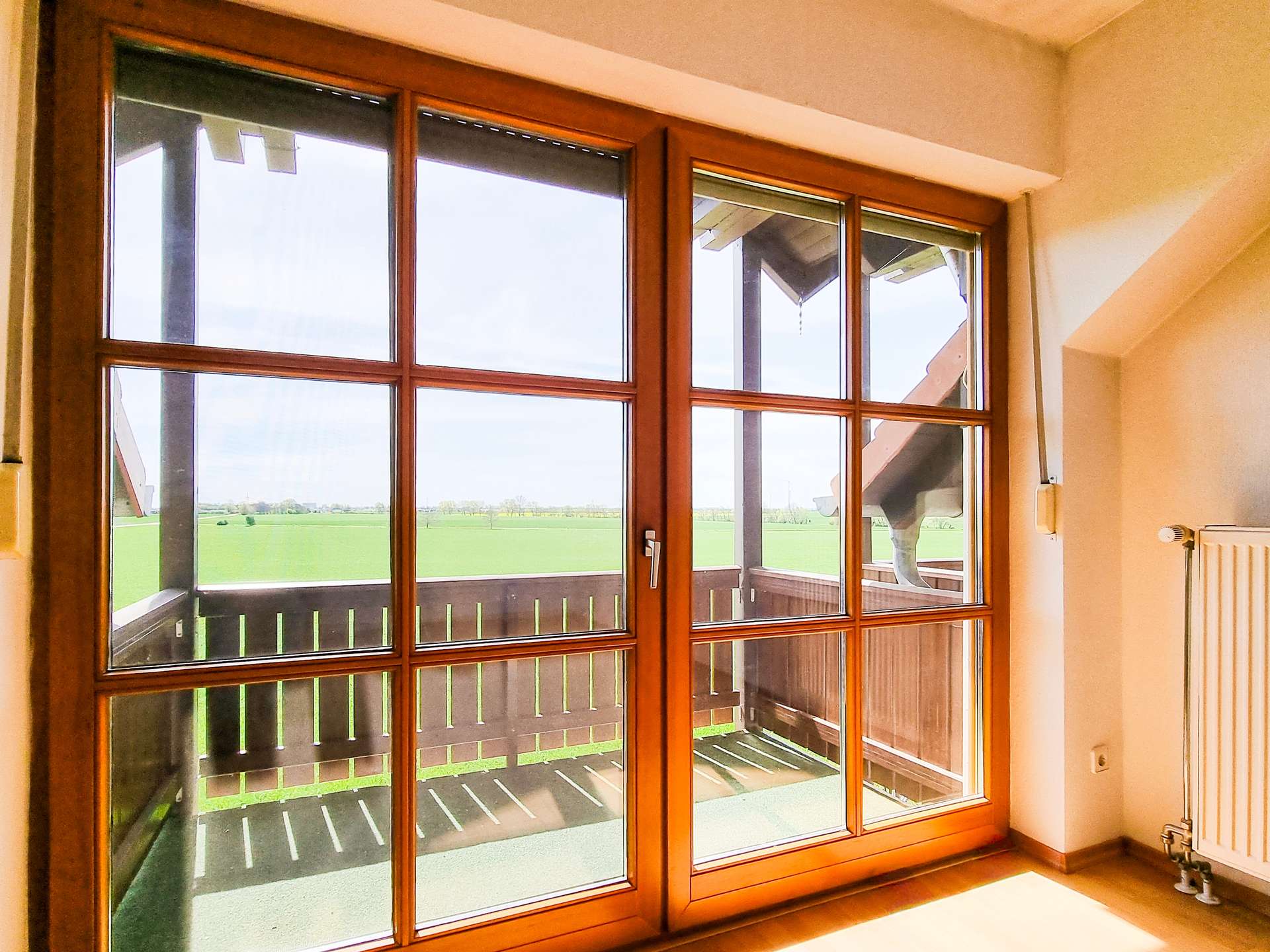 Interior view of large wooden-framed windows letting in sunlight, with green fields visible outside.