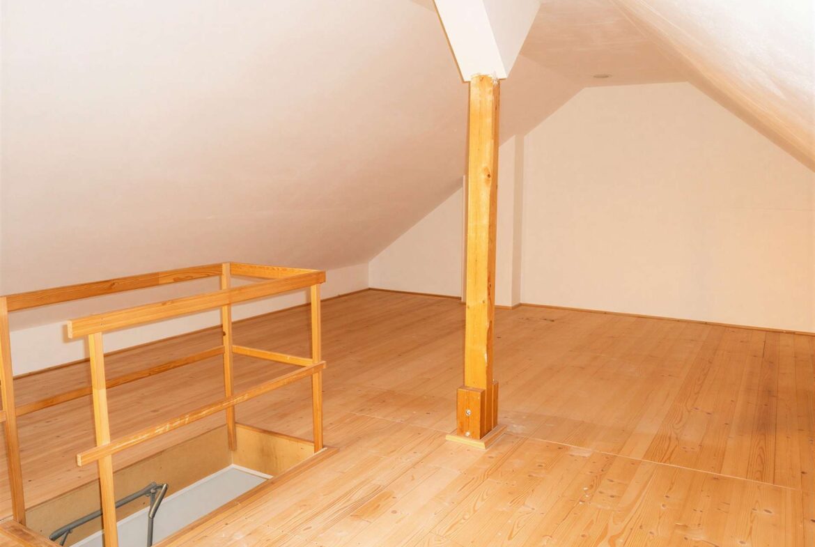 Attic space with light wood floors, sloped ceilings, and a wooden railing surrounding an open stairwell down to the lower level.