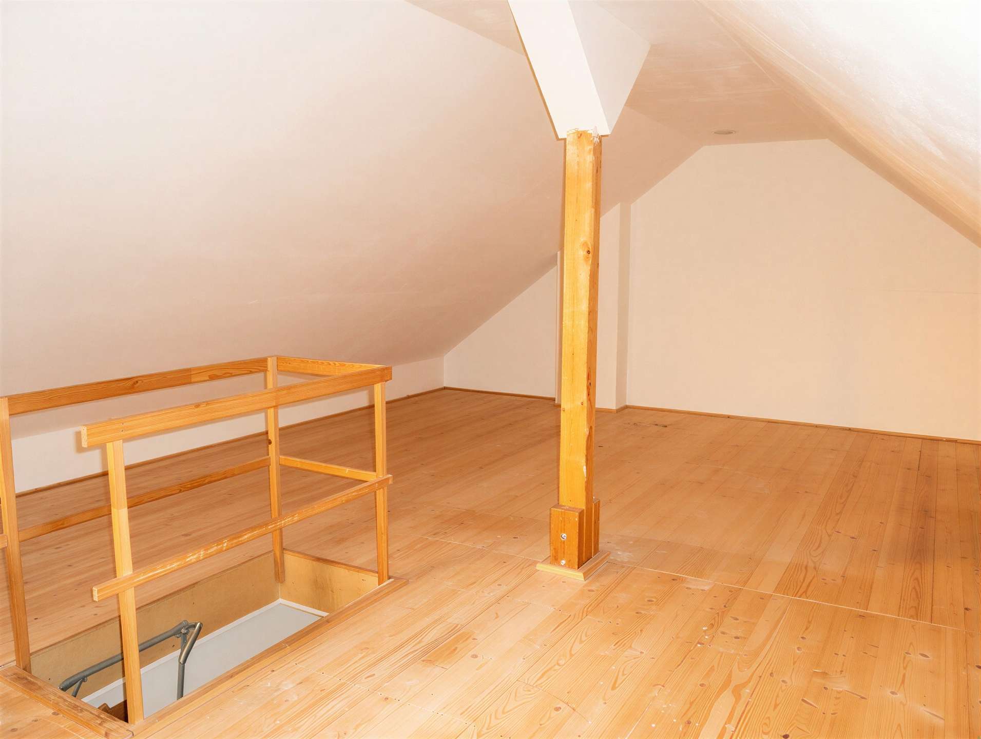 Attic space with light wood floors, sloped ceilings, and a wooden railing surrounding an open stairwell down to the lower level.