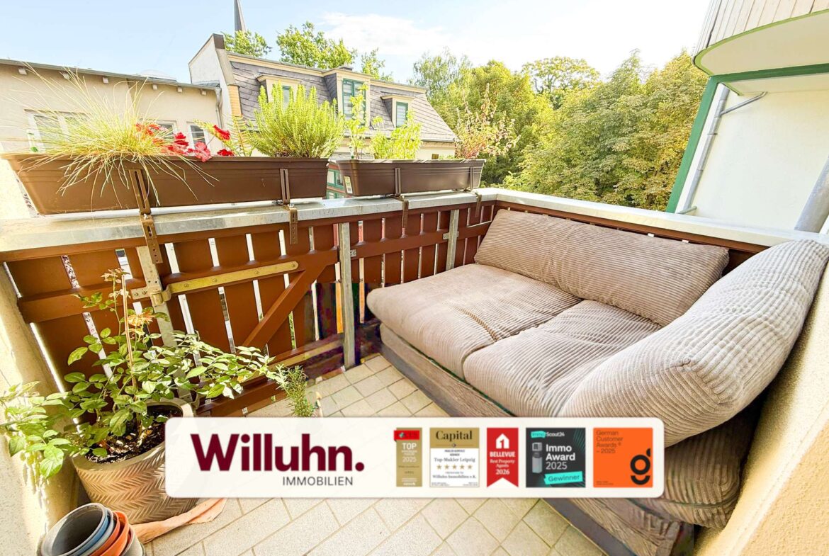 Cozy balcony with beige cushioned seating, potted plants along the railing, and a Willuhn Immobilien banner at the bottom.