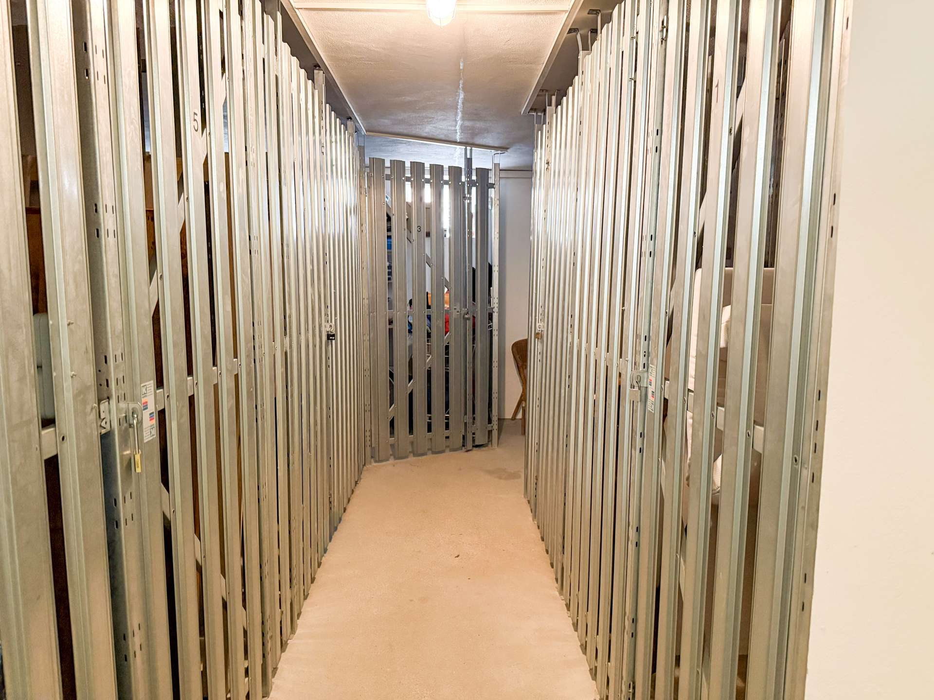 Narrow hallway of metal storage lockers with numbered doors on both sides.