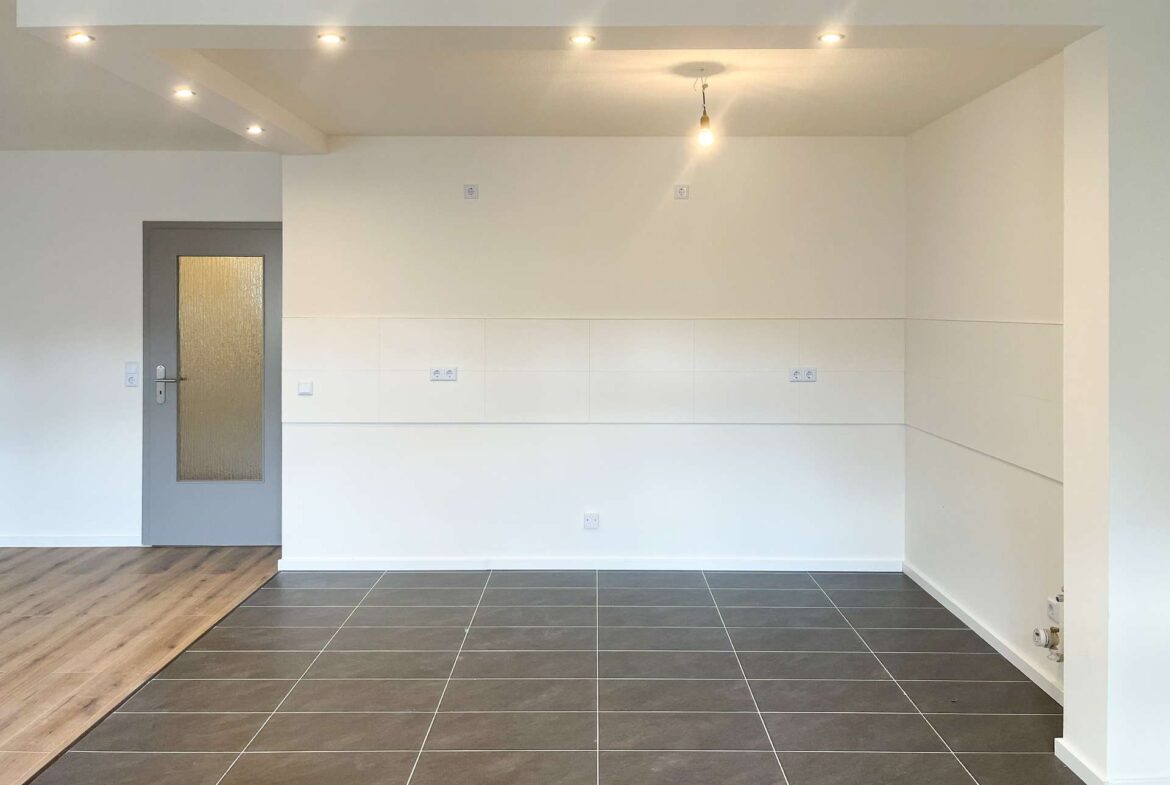 Empty modern interior with wood flooring along a step, dark tiled area, white walls, a gray door with frosted glass, and a hanging bulb.