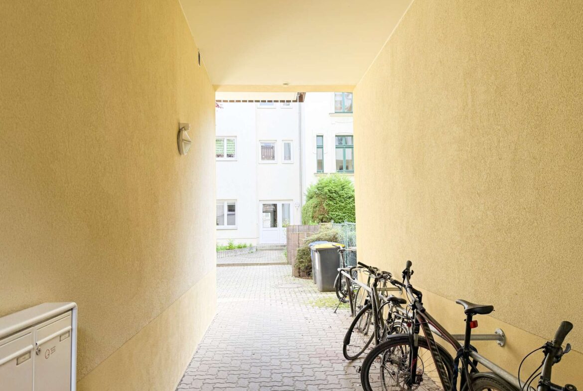 Narrow passage between yellow walls with parked bicycles on the right and a white building at the end.