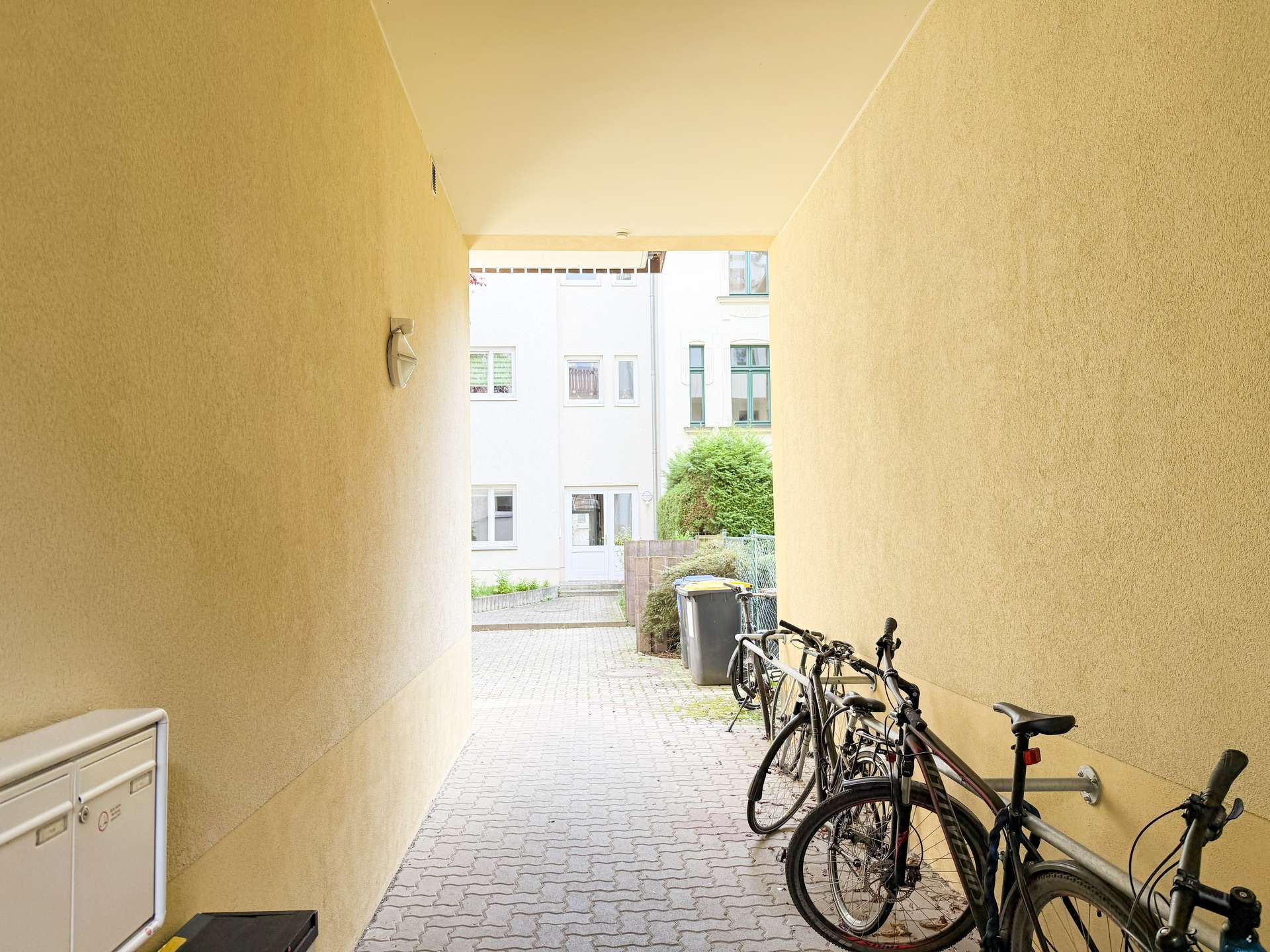 Narrow passage between yellow walls with parked bicycles on the right and a white building at the end.