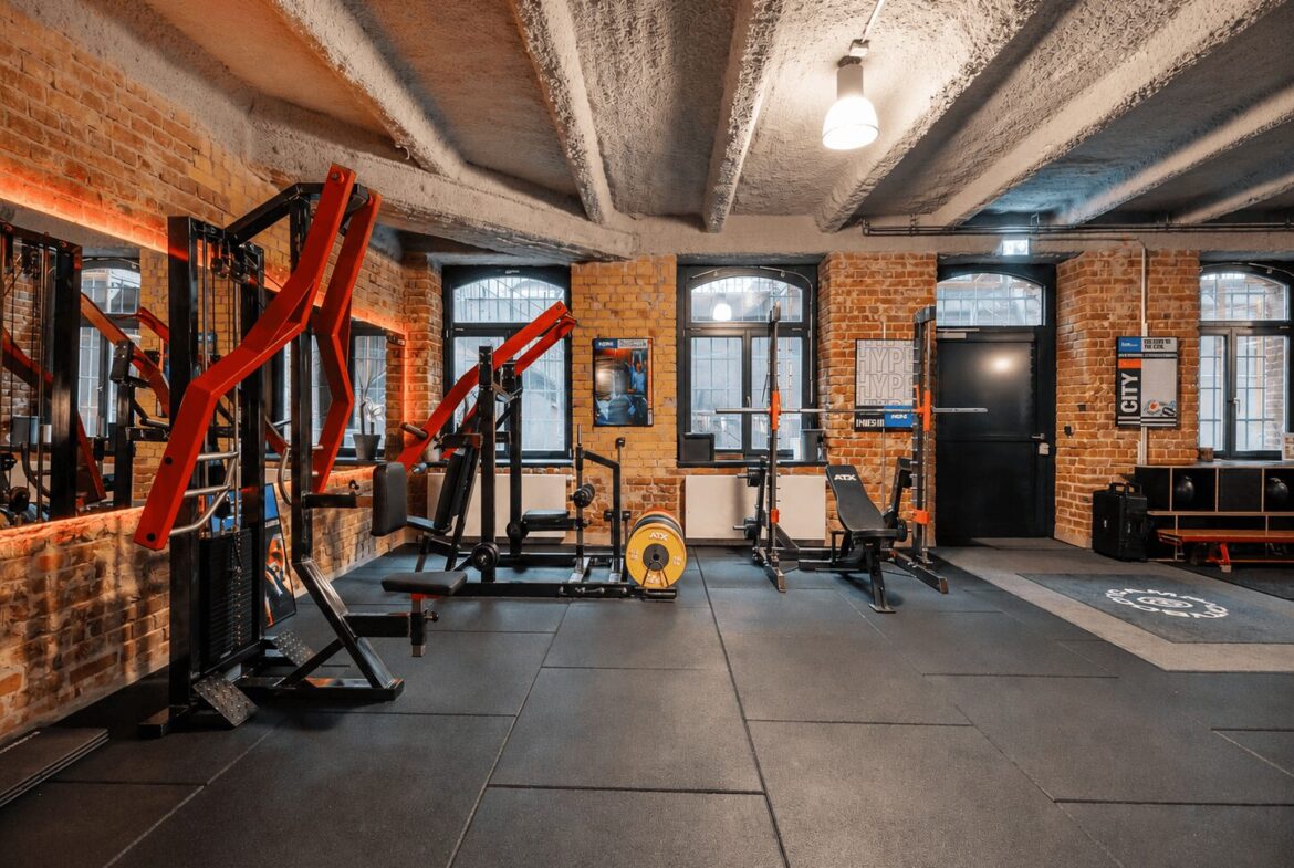 Industrial gym with exposed brick walls, red weight machines, benches, and a yellow weight plate on the floor.