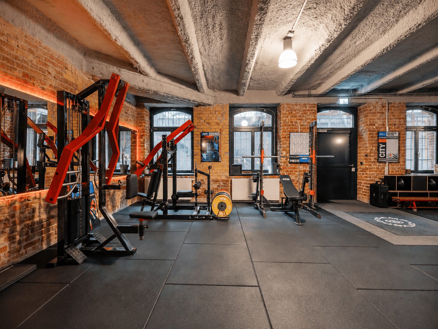 Industrial gym with exposed brick walls, red weight machines, benches, and a yellow weight plate on the floor.