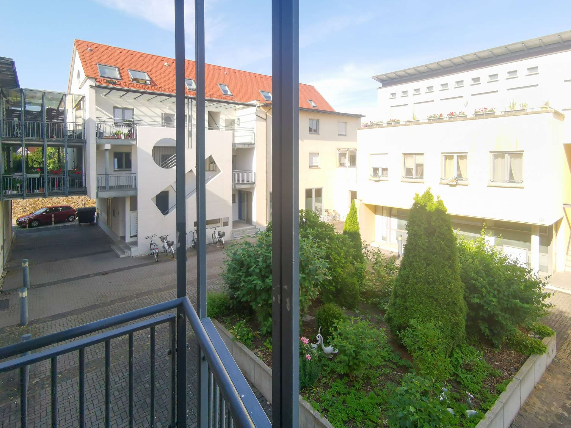 View from a balcony overlooking a residential courtyard with white buildings, red-tiled roofs, and greenery.