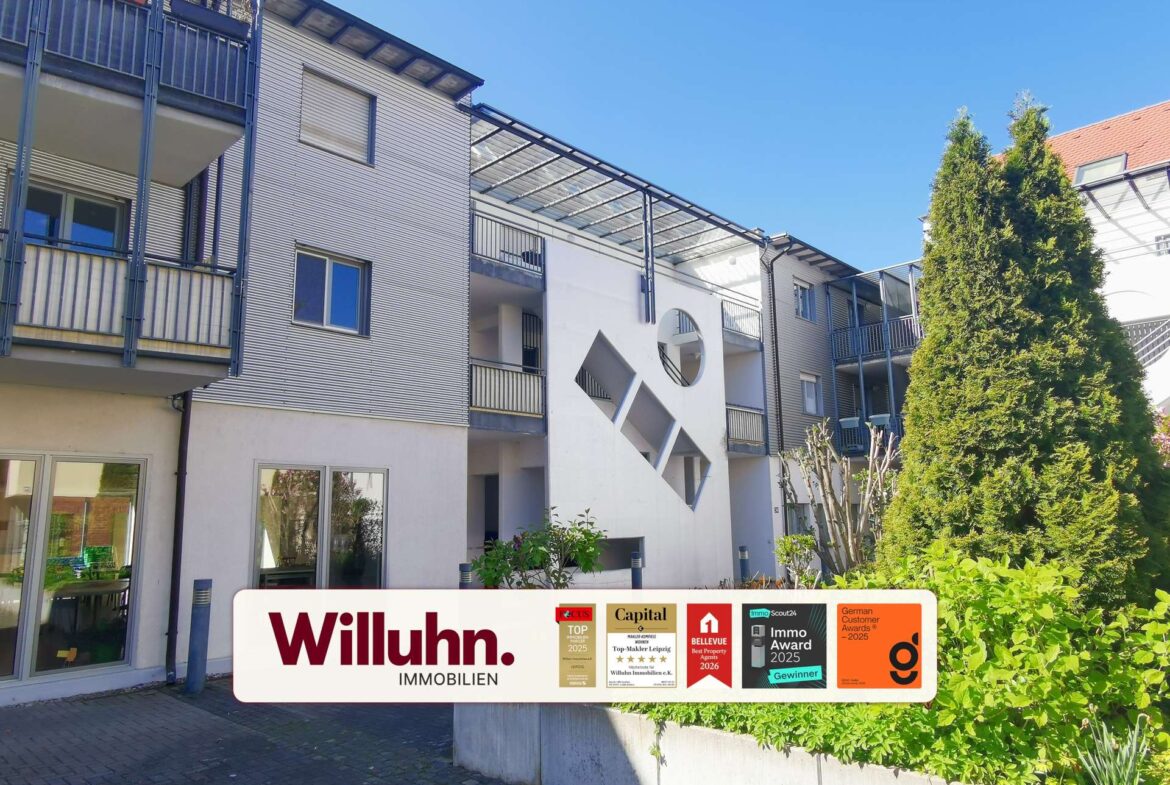 Modern apartment building with glass-walled walkways and a large Willuhn Immobilien sign featuring awards on the front.
