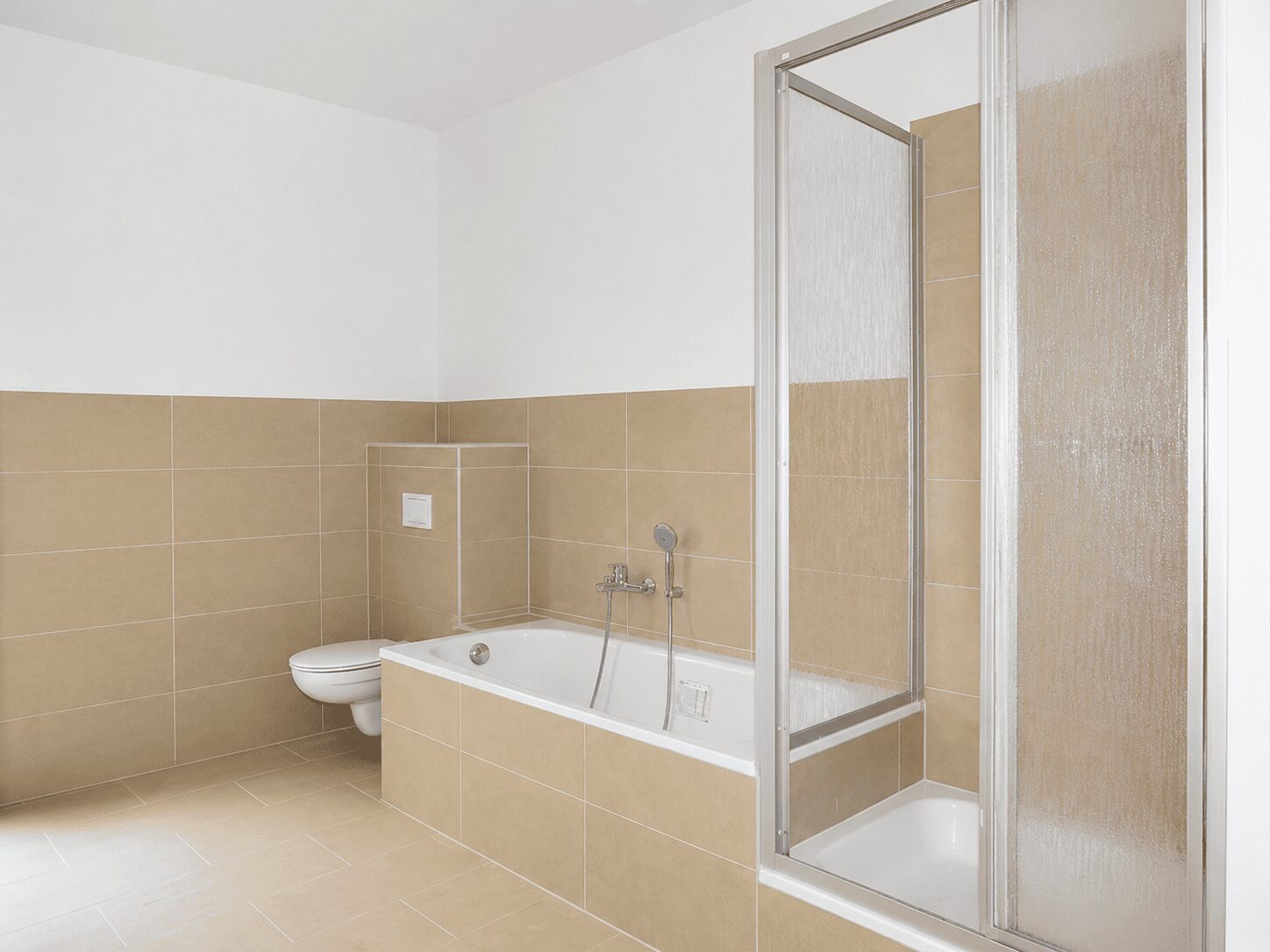 Bathroom with beige tile walls and floor, featuring a white built-in bathtub, wall-mounted toilet, and glass-front shower enclosure on the right.