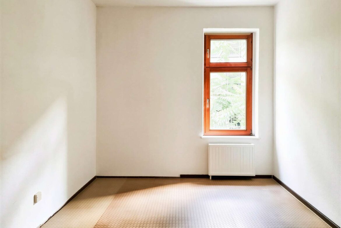 Room interior with beige walls, a single wooden-framed window, and a white radiator beneath it