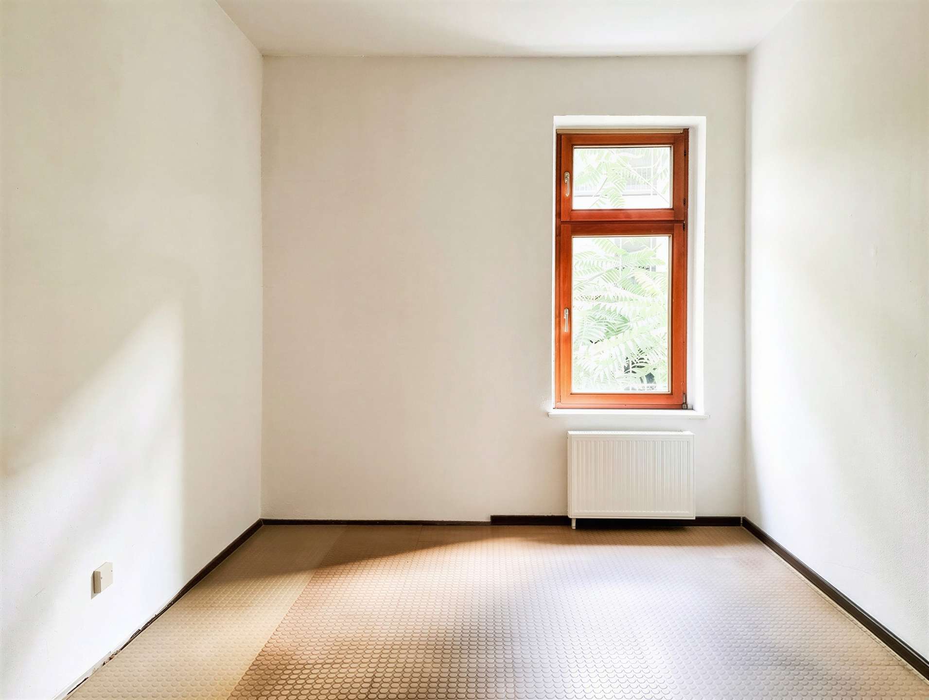 Room interior with beige walls, a single wooden-framed window, and a white radiator beneath it