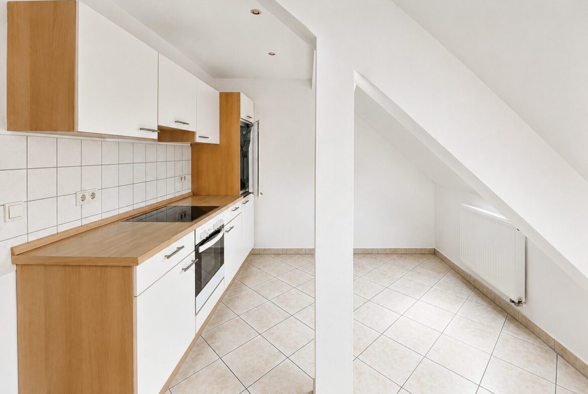 Bright, L-shaped kitchen with white cabinets, light wood countertops, and tiled backsplash; built-in oven and cooktop under a sloped ceiling.