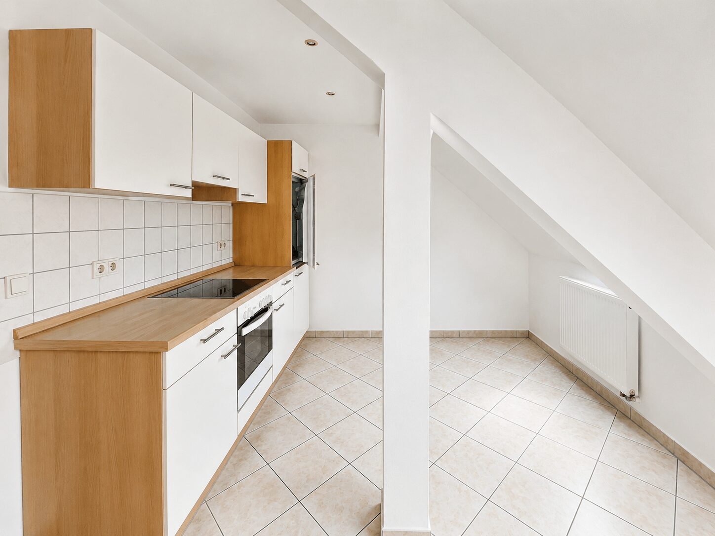 Bright, L-shaped kitchen with white cabinets, light wood countertops, and tiled backsplash; built-in oven and cooktop under a sloped ceiling.