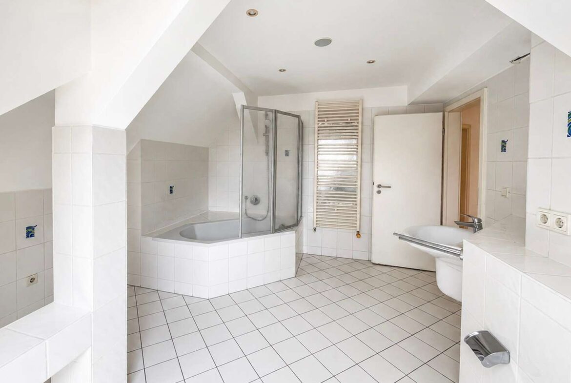 Bright white bathroom with a corner bathtub, glass shower enclosure, towel radiator, and wall-mounted sink.
