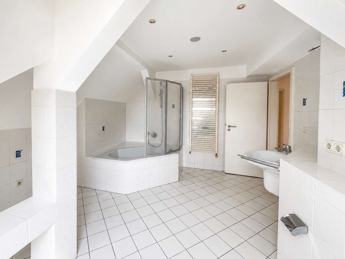 Bright white bathroom with a corner bathtub, glass shower enclosure, towel radiator, and wall-mounted sink.
