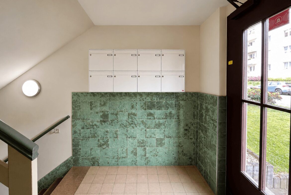 Stairwell landing with a row of white mailboxes above a green tiled wall and a glass door to the outside.