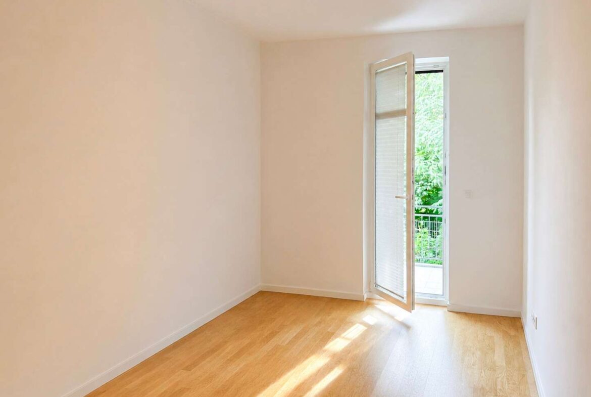 Bright empty room with light wood flooring and an open glass door leading to a green outdoor balcony area